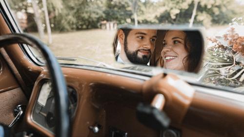 Mariés dans le reflet du rétroviseur de leur voiture vintage